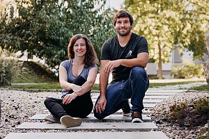 Ein Mann und eine Frau, leger im T-Shirt gekleidet, sitzen im Freien und lächeln in die Kamera