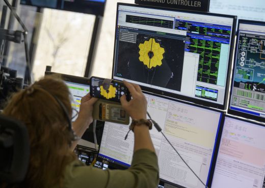 NASA Mitarbeiter im Control Room vor einem Bildschirm, der das Webb Teleskop zeigt 