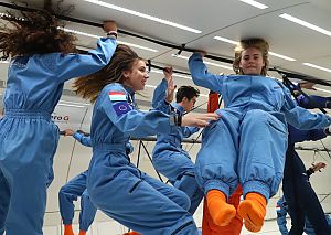 Jugendliche in hellblauen Overalls die ineinem weißen Raum den Zustand der Schwerelosigkeit genießen.
