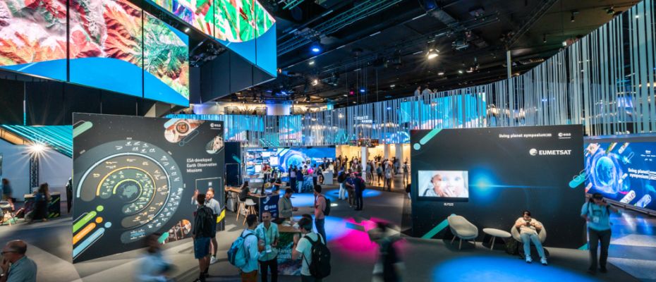 Copyright: ESA/JMai Ein Ausstellungsraum voller Besucher:innen und mit vielen bunten Bildern und Animationen zu Weltraumthemen