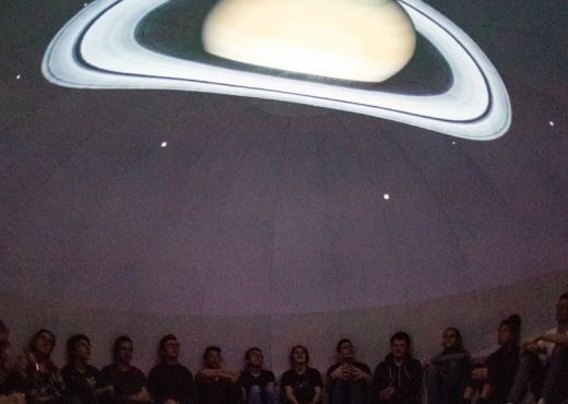 Children sit in a darkened room on the floor with Saturn projected onto the ceiling above them.