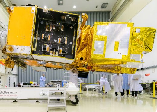 Satellit in einer Halle, eingehüllt in golener Thermaisolation und Personen die daran arbeiten..