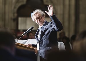 Ludwig Möller steht an einem Rednerpullt und winkt in die Kamera und in das Publikum.