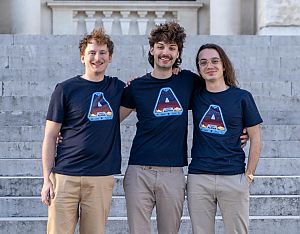 Drei junge Männer auf einer Stiege, die idente dunkelblaue T-Shirts mit dem Aufdruck A - Oasis Alpha tragen