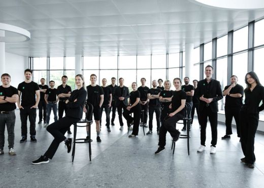21 smiling, young men and women in black dresses in a large, light room