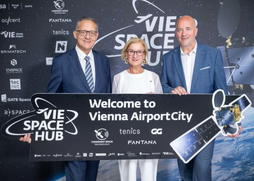 Zwei ältere Männer im blauen Anzug und Landeshauptfrau Mikl-Leitner in weißer Bekleidung halten zusammen ein dunkelblaues Transparent mit weißen Aufschriften "VIE SPACE HUB - Welcome to Vienna City Airport", einem Satellitenbild und diversen Firmenlogos, der Inhalt des Tranparents ist auch in größerer Form als Bildhintergrund sichtbar.